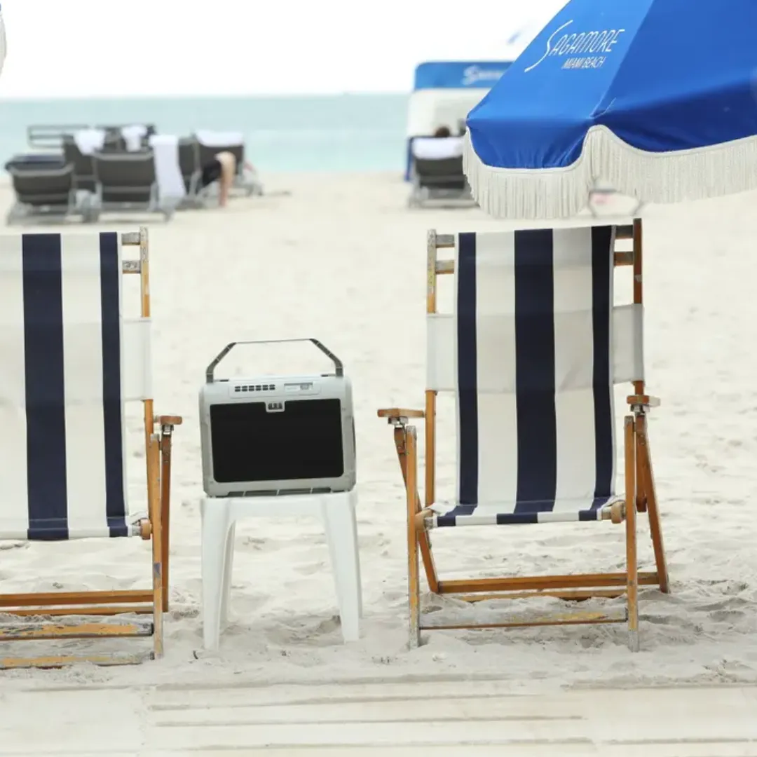 Portable gun safe on a beach chair at the shoreline with striped umbrella and Adirondack chairs